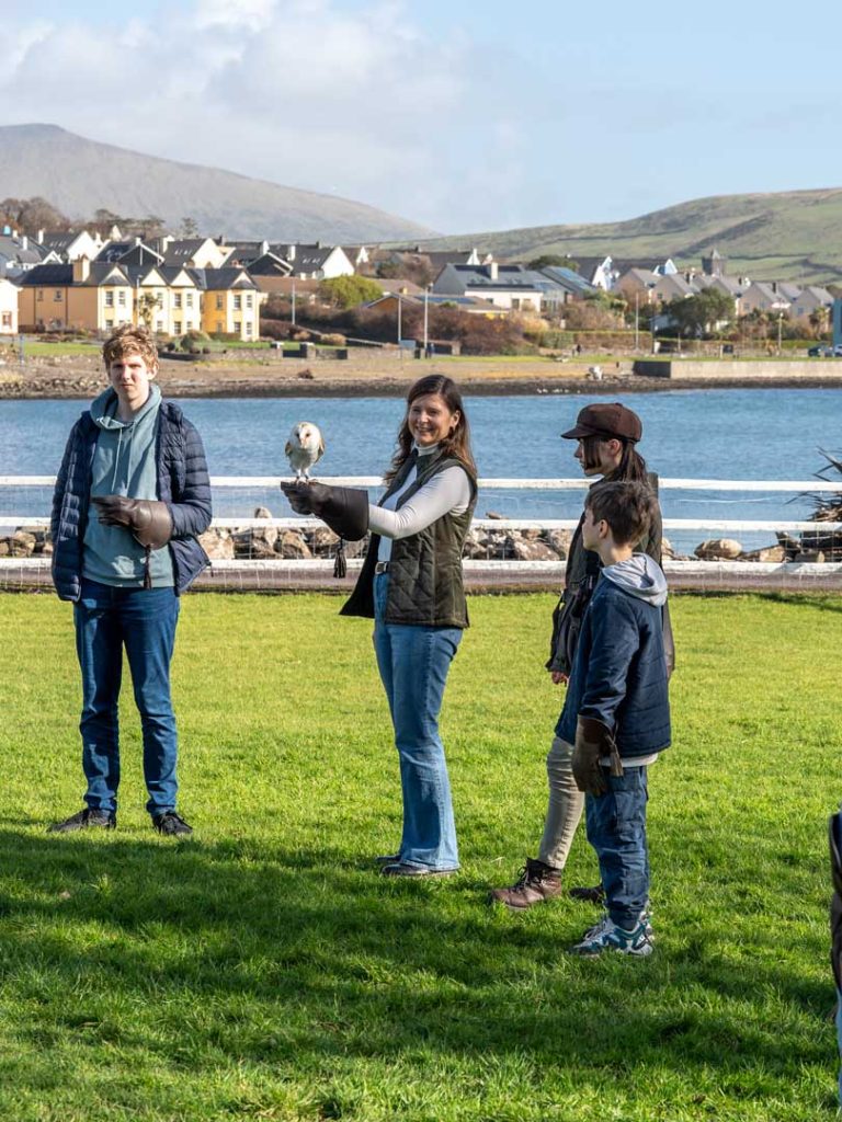 A lady holding an owl in front of dingle bay with her family onlooking